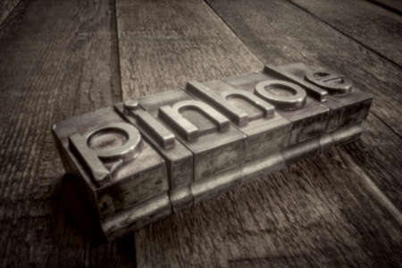 pinhole word in gritty letterpress metal type over weathered wood, soft focus image shot with...