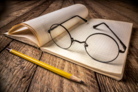 Vintage blank notebook or journal on a rustic picnic table with reading glasses, soft focus image shot with lensless pinhole cameraの写真素材