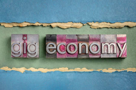 gig economy word abstract in gritty letterpress metal type against handmade paper, business and finance conceptの写真素材