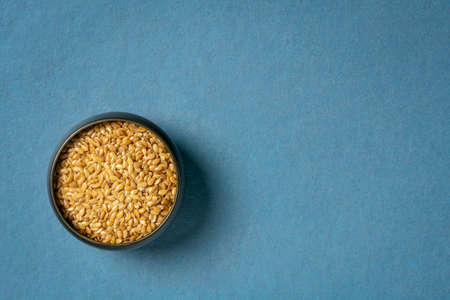 golden flax seeds in a small ceramic bowl, top view on a blue handmade paper with a copy space, superfood supplement and ingredientの写真素材