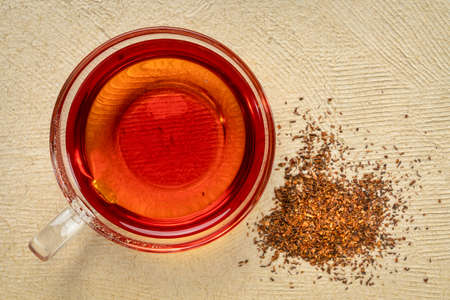 rooibos red tea  -  a glass cup of a hot drink and loose leaves, tea made from the South African red bush, naturally caffeine freeの写真素材