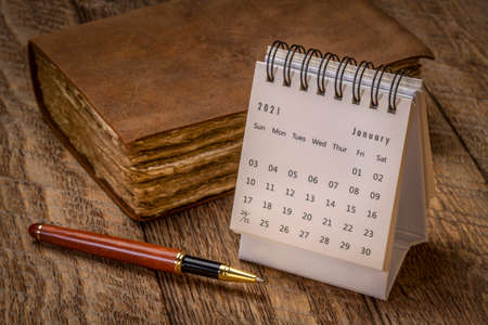 January 2021- spiral desktop calendar against rustic wood with an antique leather-bound journal and a stylish pen, season,  time and business conceptの写真素材