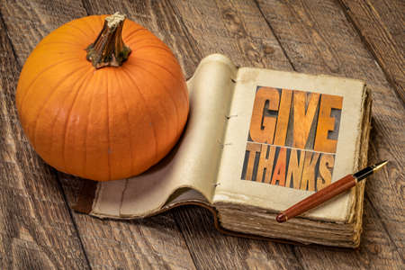 give thanks - word abstract in vintage letterpress wood type in a retro journal with pumpkin against...