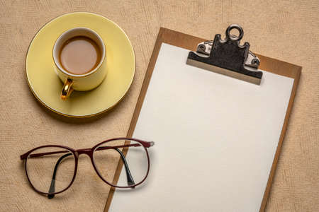 business desktop concept - clipboard with blank paper,reading glasses and a cup of coffee against textured paperの写真素材