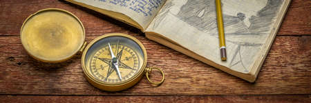 Vintage brass compass and old travel journal with handwriting and pencil sketches (property release attached), travel concept.の写真素材