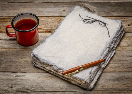 retro sketchbook with gray toned heavyweight deckle edge paper sheets with a stylish pen and a cup of tea against rustic weathered woodの写真素材
