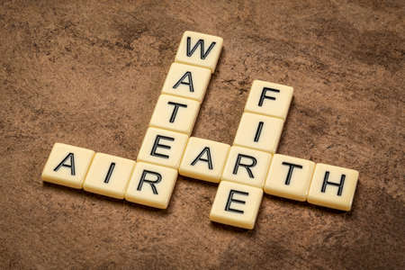 water, earth, air and fire crossword in ivory letter tiles against textured handmade paper, four elements of classic Greek philosophyの写真素材