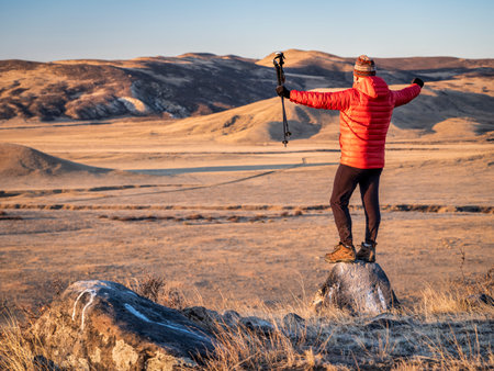 happy male hiker with trekking post at foothills of  Rocky Mountains in northern Colorado - fall scenery at sunrise in Soapstone Prairie Natural Area near Fort Collinsの写真素材