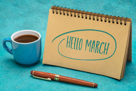 Hello March! Handwriting in a spiral notebook with a cup of coffee and  a pen.