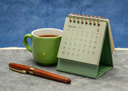 March 2021 - spiral desktop calendar against abstract paper landscape with a cup of coffee and pen, time and business conceptの写真素材