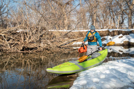 senior male paddler is launching an inflatable whitewater kayak on a small river - Poudre River in Fort Collins, Colorado, winter or early spring sceneryの写真素材