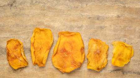 slices of dried mango fruit against textured bark paper with a copy spaceの写真素材