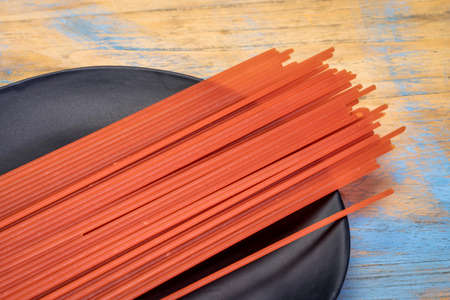 gluten and grain free Italian spaghetti pasta sourced from red lentil flour, black plate against rustic woodの写真素材