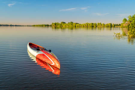 stand up paddleboard is floating on a calm lake - Boyd Lake State Park in northern Colorado, morning...