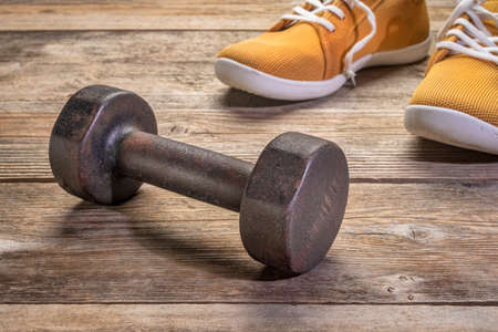iron dumbbell with sneakers with barefoot sneakers on a rustic wooden deck, fitness conceptの写真素材