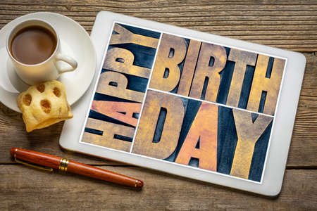 Happy birthday - greeting card in vintage letterpress wood type on a digital tablet with a cup of coffee against rustic woodの写真素材