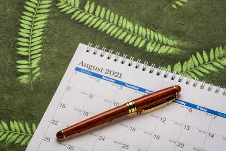 August 2021 - spiral desktop calendar against green mulberry paper with leaf inclusions, time and business conceptの写真素材