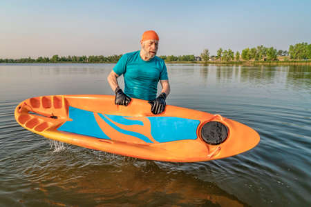athletic, senior man with a prone kayak on a lake in Colorado, this water sport combines aspects of...