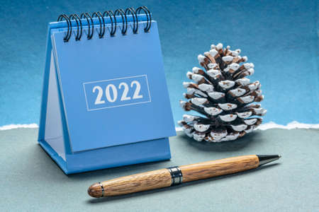 2022 spiral desktop calendar with a decorative frosty pine cone against handmade paper, New Year, time management and business conceptの写真素材
