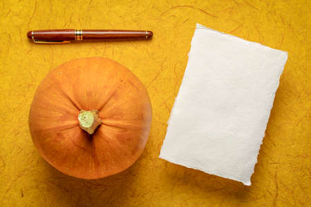 small sheet of blank white Khadi rag paper against dark yellow gampi paper, with a pumpkin and a stylish pen, fall holidays themeの写真素材