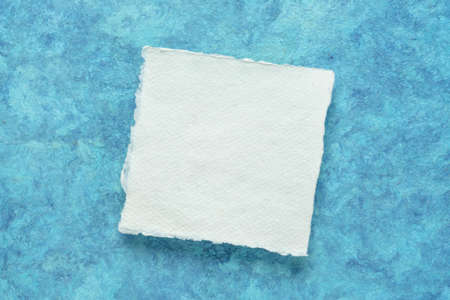small square sheet of blank white Khadi paper against blue amate bark paperの写真素材