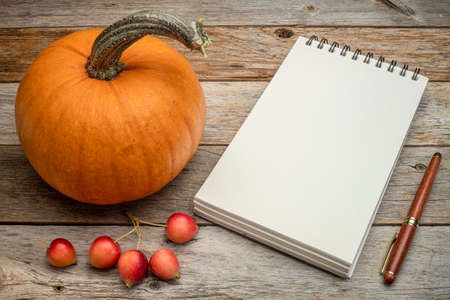 blank spiral notebook with pumpkin and crab apples on a rustic wooden table, Halloween or Thanksgiving themeの写真素材