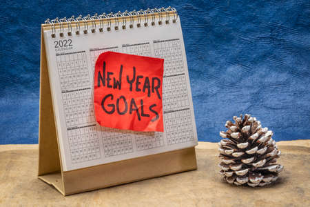 New Year goals - reminder note on the 2022 year spiral desktop calendar with a frosty pine cone...