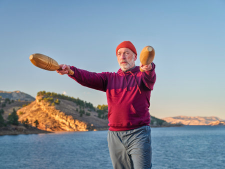senior man is exercising with wooden Indian clubs outdoors on a lake shore in Colorado, Horsetooth Reservoir in fall sceneryの写真素材