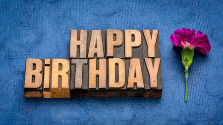 Happy Birthday greeting card in vintage letterpress wood type with a carnation flower against handmade bark paperの写真素材
