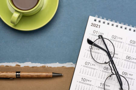 2021 spiral desktop calendar with a cup of coffee against handmade paper, time management and...