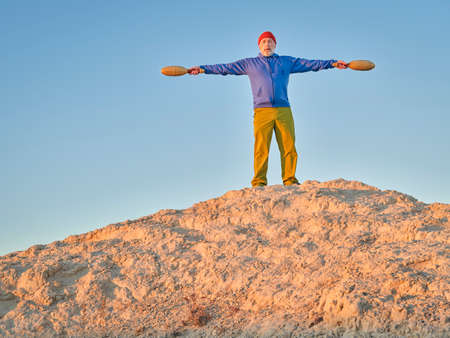 senior man is exercising with wooden Indian clubs outdoors outdoors at sunset on Colorado prairieの写真素材
