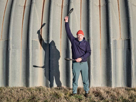 senior athletic male is exercising with Indian clubs with a company of a shadow on a grunge metal hangar, workout in urban or industrial environmentの写真素材