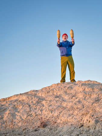 senior man is exercising with wooden Indian clubs outdoors outdoors at sunset on Colorado prairieの写真素材