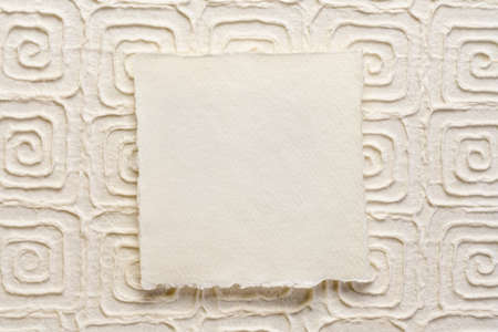 small square sheet of blank white Khadi paper against heavy embossed mulberry paper with Greek key patternの写真素材