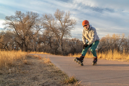 inline skating on a paved bike trail along Poudre River in Fort Collins, Colorado - senior male skater is stopping using a hill brake, fall or winter sceneryの写真素材