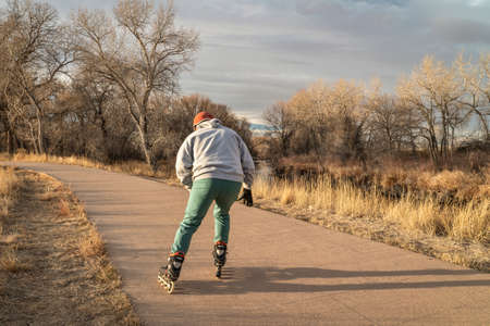 senior male  is inline skating on a paved bike trail along Poudre River in Fort Collins, Colorado, fall or winter sceneryの写真素材
