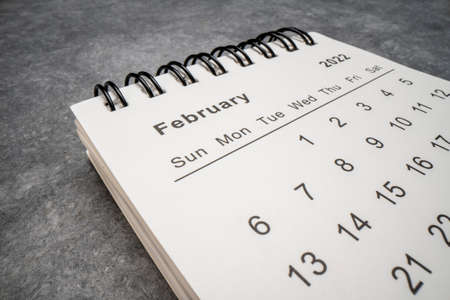 February 2022 - spiral desktop calendar  against gray textured paper, time and business concept,...