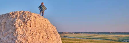 Man in a Mexican poncho and cowboy hat is enjoying summer sunrise at prairie - Pawnee National Grassland in Colorado, panoramic web bannerの写真素材