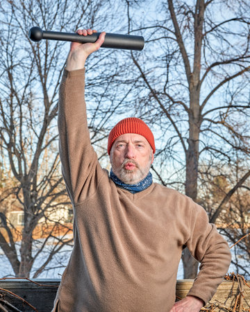 senior man (in late 60s) is exercising with a steel indian club in his backyard, winter afternoon, fitness over 60 conceptの写真素材