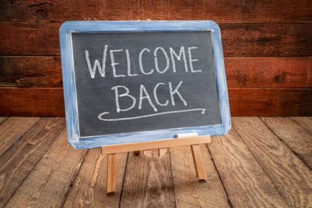 welcome back - white chalk handwriting on a slate blackboard, easel sign against rustic, weathered wood, hospitality and business conceptの写真素材