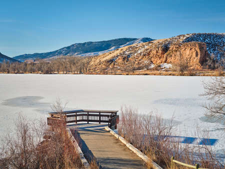 Early winter morning at Colorado foothills near Fort Collins - frozen Watson Lake with a fishing pier and Front Range of Rocky Mountainsの写真素材