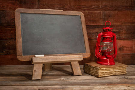blank slate blackboard easel sign on a rustic weathered wood with old book and oil lantern, retro classroom conceptの写真素材