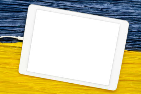 mockup of digital tablet with a blank isolated screen (clipping path included) against paper abstract in colors of Ukraine national flag, blue and yellowの写真素材
