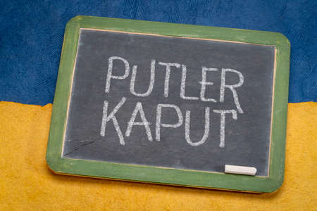Putler kaput - sign against Russian attack on Ukraine, white chalk writing on a slate blackboard against paper abstract in color of Ukrainian national flag, blue and yellowの写真素材