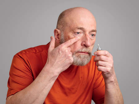 senior man is applying a retinol cream under his eyes, skincare and self care for men conceptの写真素材