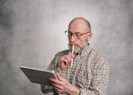 casual portrait of bald, bearded senior man working on a digital tablet with electronic pencilの写真素材