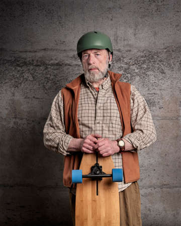 casual portrait of a bearded senior man with a long cruising skateboard against grunge wallの写真素材