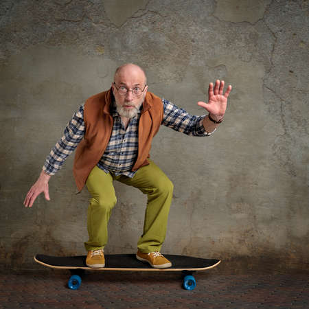 scared bearded senior man riding long skateboard in a grunge urban environmentの写真素材
