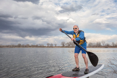 happy senior male paddler on a stand up paddleboard, lake in Colorado in early spring sceneryの写真素材