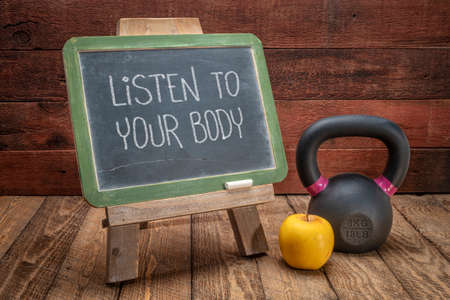 Listen to your body reminder -  slate blackboard sign against weathered red painted barn wood with a kettlebell, wellbeing and fitness conceptの写真素材